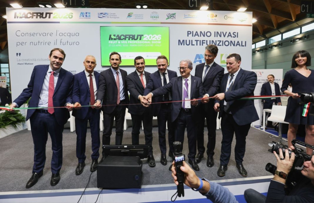 Group of men in suits cutting a red ribbon at a trade show, with a backdrop showing NACFRUT 2026 and 'Piano Invasi Multifunzionali' banner.