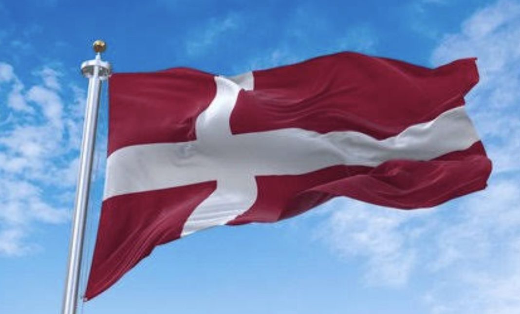 Danish flag waving on a flagpole against a blue sky.